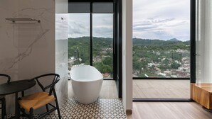 Une salle de bain moderne avec une baignoire sur pieds, une chaise noire et une vue sur le paysage urbain à travers de grandes fenêtres.