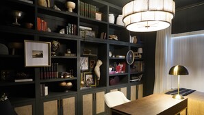 Een moderne kamer met een donkergroene boekenkast, gevuld met boeken, decoratieve items en een ingelijst kunstwerk. Een houten bureau met een messing lamp staat voor de boekenkast.