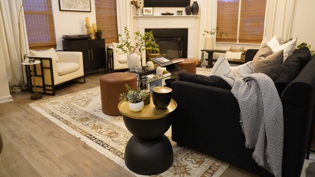 Een woonkamer met een zwarte bank, een salontafel, een open haard en een televisie erboven.
