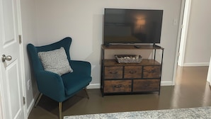 Un sillón color turquesa con un cojín estampado de leopardo, un mueble de televisión de madera y estantes decorativos arriba.