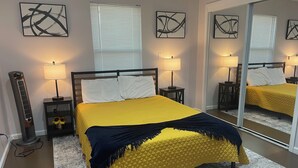 Un dormitorio con cama, dos mesitas de noche, un calentador y obras de arte en las paredes.