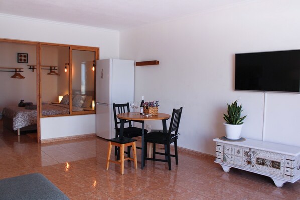 Un espacio habitable compacto con comedor, cama, refrigerador, televisor y un mueble con una planta.