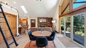 Uma sala de estar espaçosa com uma janela grande, uma lareira e um espaço de refeições com uma mesa redonda e cadeiras.