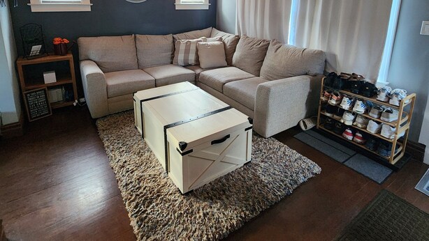 A living room with a sectional sofa, a coffee table, a shoe rack, and a clock on the wall.