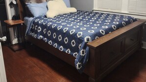 A bedroom with a wooden bed, a nightstand, a lamp, and a window with blinds.