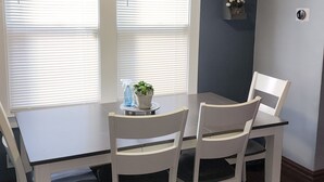 A dining area with a table and four chairs, a ceiling fan, and a wall-mounted shelf with flowers.