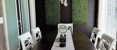 Un comedor con una mesa de madera oscura, sillas blancas, una lámpara colgante y adornos de pared verdes.
