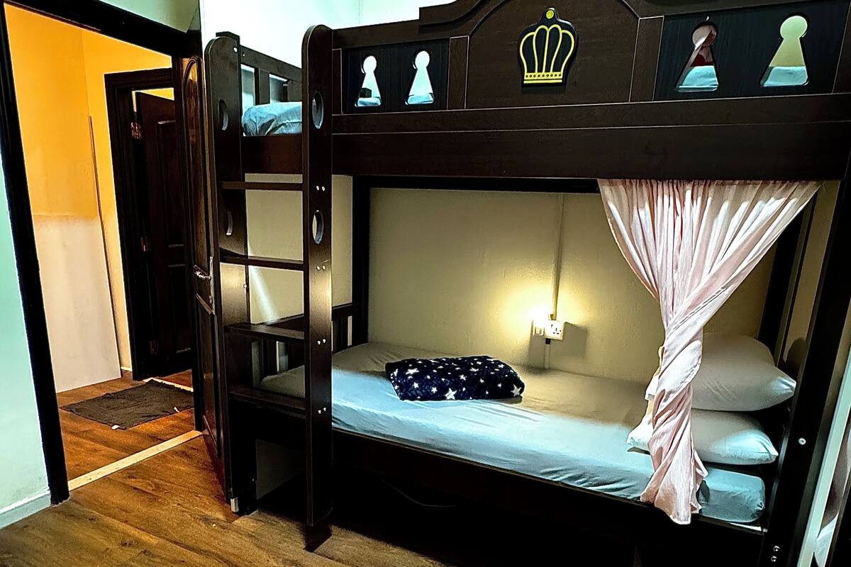 A bunk bed with a canopy, a bedside table with a lamp, and a window with curtains.