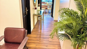 A hallway with a brown leather chair, a glass table with a vase and flowers, and a potted plant. - Happy Hostel Dubai (Dubai)