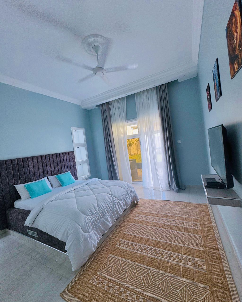 A bedroom with a bed, a ceiling fan, a TV, and a window with curtains.