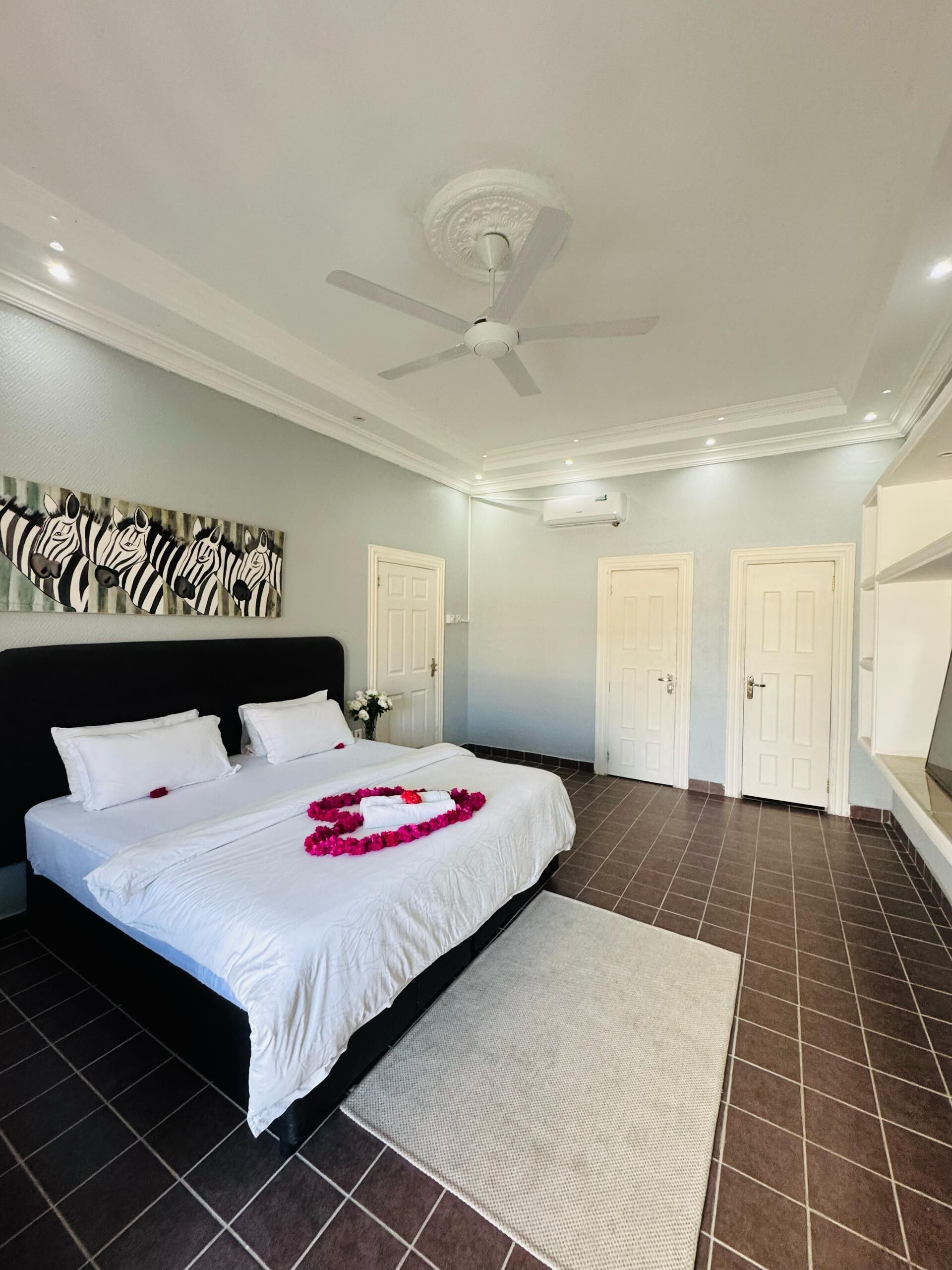 A spacious bedroom with a large bed, a ceiling fan, and a zebra-themed wall art.
