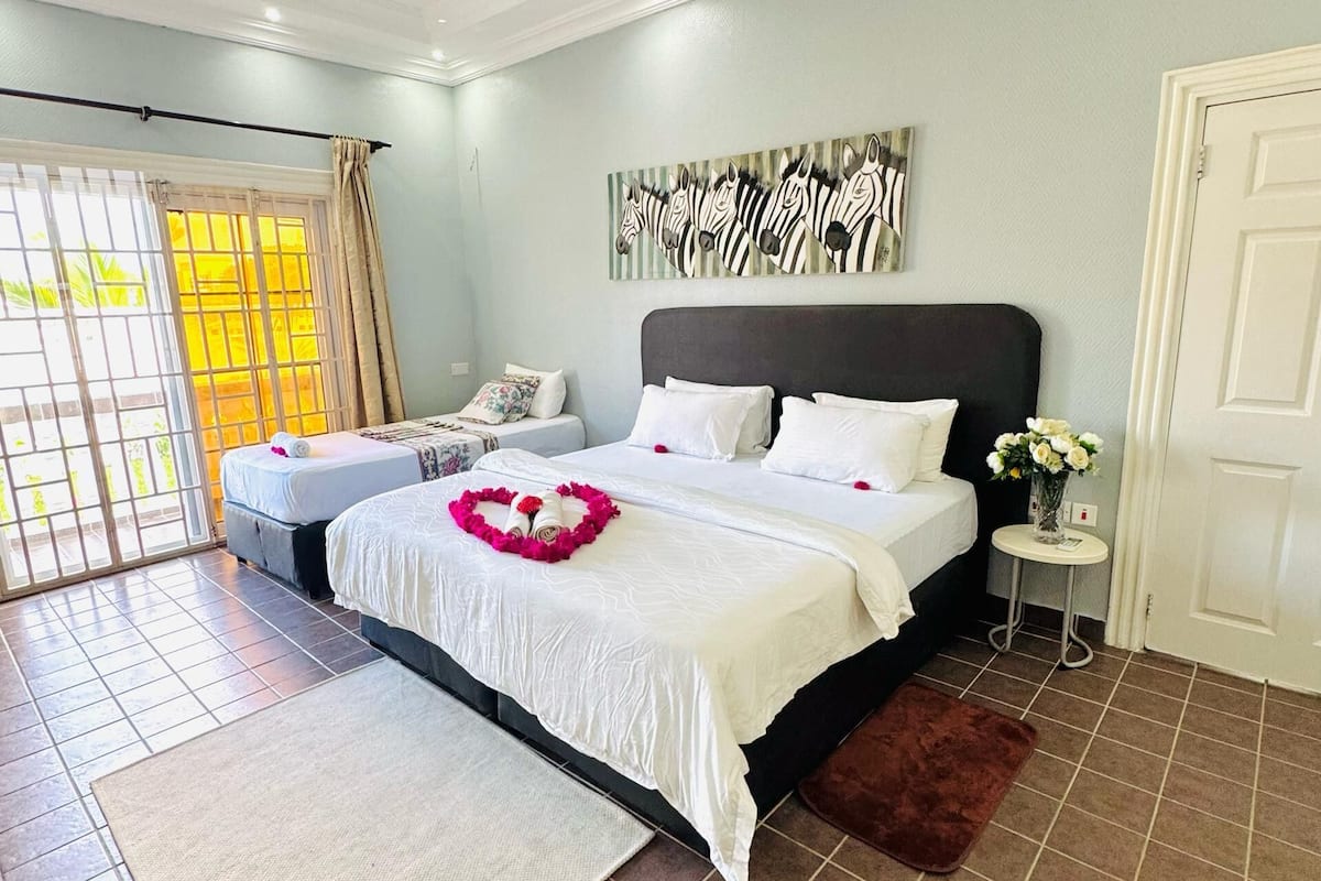A bedroom with a bed, a ceiling fan, a window with curtains, a wall art piece, and a door.