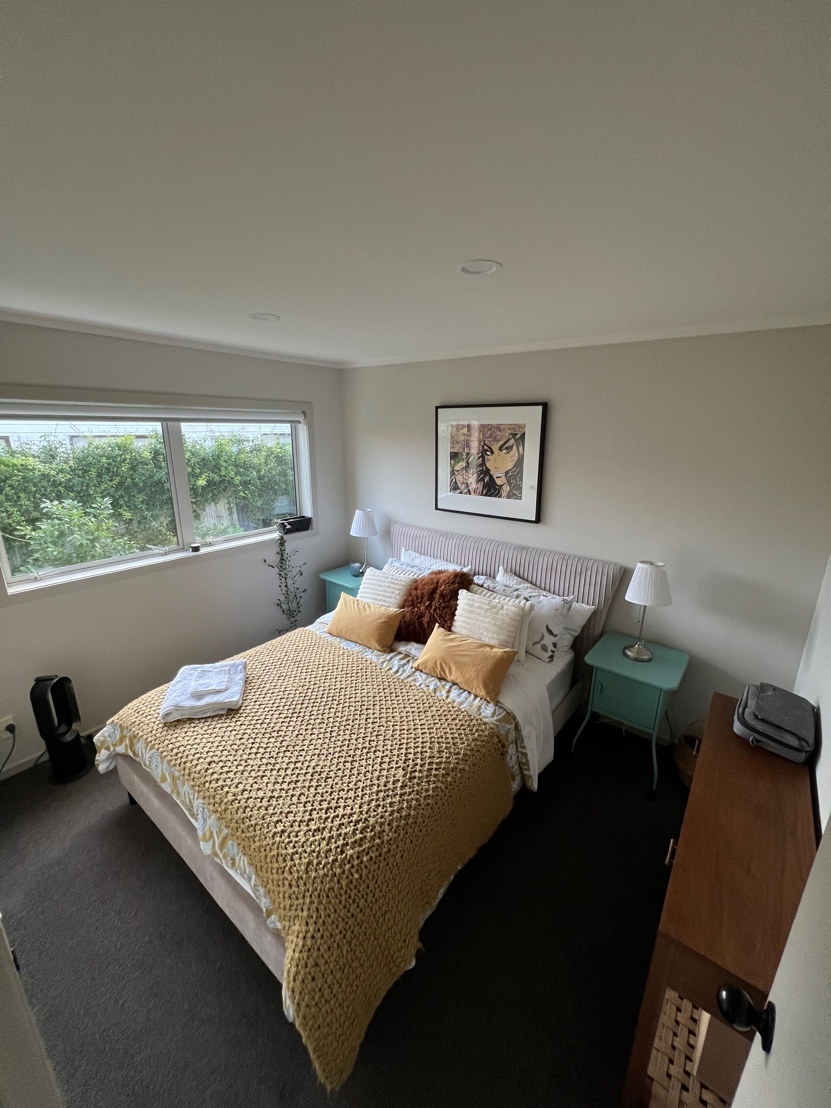 A bedroom with a large bed, a window, a bedside table, a lamp, and a framed picture on the wall.