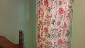 Ein Schlafzimmer mit einem hölzernen Bettgestell, einer blumigen Tagesdecke und einem Fenster mit floralem Vorhang.