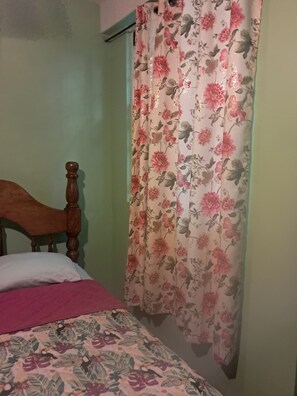 Une chambre à coucher avec un cadre de lit en bois, une couvre-lit à motifs floraux et une fenêtre ornée d’un rideau à fleurs.