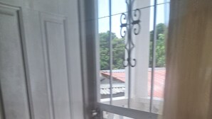 Eine Tür mit einem Metallgitter, das zu einem Außenbereich mit Fliesen und Blick auf ein Gebäude mit rotem Dach führt.