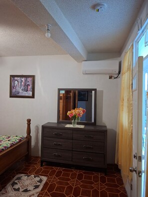 A bedroom with a bed, a dresser with a mirror, a wall-mounted air conditioner, and a tiled floor.