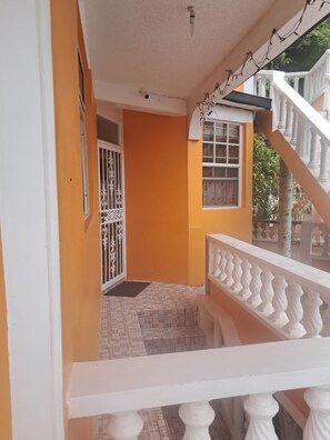 Un espace extérieur abrité, doté d'une rambarde blanche, d'une porte ornée de barreaux en métal et d'un sol carrelé.