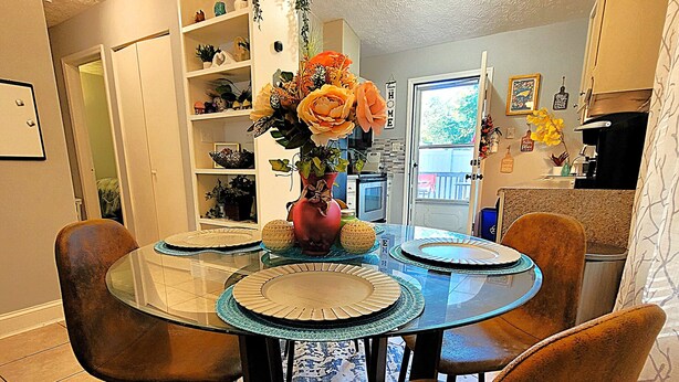 A dining area with a glass-top table, four chairs, and a vase of flowers. - Cozy and Bright Retreat Near Raleigh Hotspots (Raleigh)