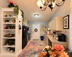 A kitchen with white cabinets, a black refrigerator, a coffee maker, and a colorful rug.