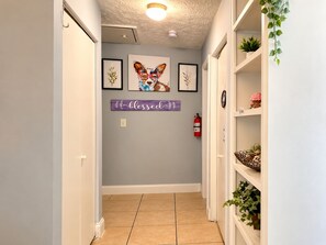 A hallway with a fire extinguisher, framed artwork, and a 'blessed' sign on the wall.