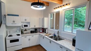 Una cocina moderna con armarios blancos, un microondas integrado, una estufa y un amplio ventanal con vistas al verdor.