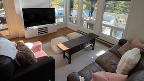 Una sala de estar moderna con un televisor grande, vigas de madera, ventanas amplias y vistas al exterior.