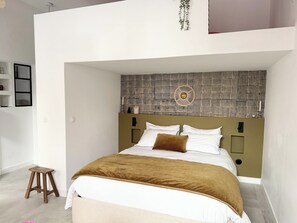 Um quarto moderno com cama, um banquinho, uma luminária fixada na parede e cabeceira estampada.