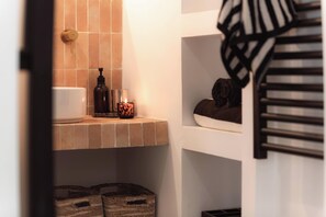 A bathroom with a tiled wall, a white sink, a bottle of soap, and a candle.