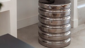 A modern, white, multi-tiered metallic trash bin in a room with a white console table and a magazine on it.