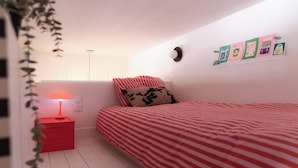A bedroom with a bed, a bedside table with a lamp, a wall clock, and some posters.