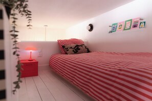 A bedroom with a bed, a bedside table with a lamp, a wall clock, and some posters.