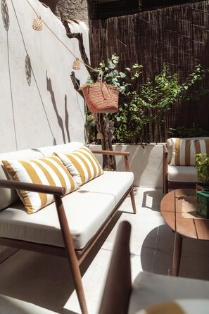A sunlit outdoor seating area with a sofa and chairs, a hanging basket, and a bamboo fence.