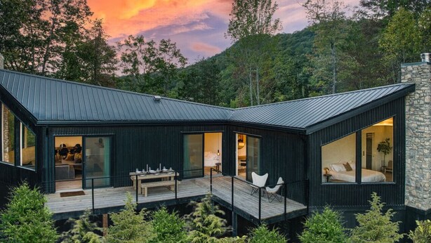 Eine moderne Holzhütte mit Terrasse, großen Fenstern und Kamin aus Stein.