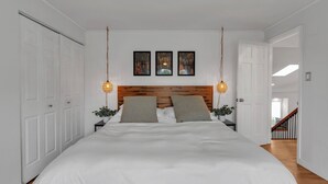 Un dormitorio con una cama grande, cabecera de madera, paredes blancas y dos mesitas de noche con lámparas.