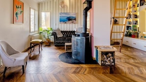 Un salon chaleureux avec un poêle à bois noir, un canapé en cuir noir, un parquet à motifs chevrons et une bibliothèque remplie de livres.