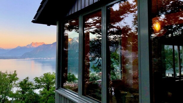 Un bâtiment doté de grandes fenêtres offrant une vue sur un lac et des montagnes.