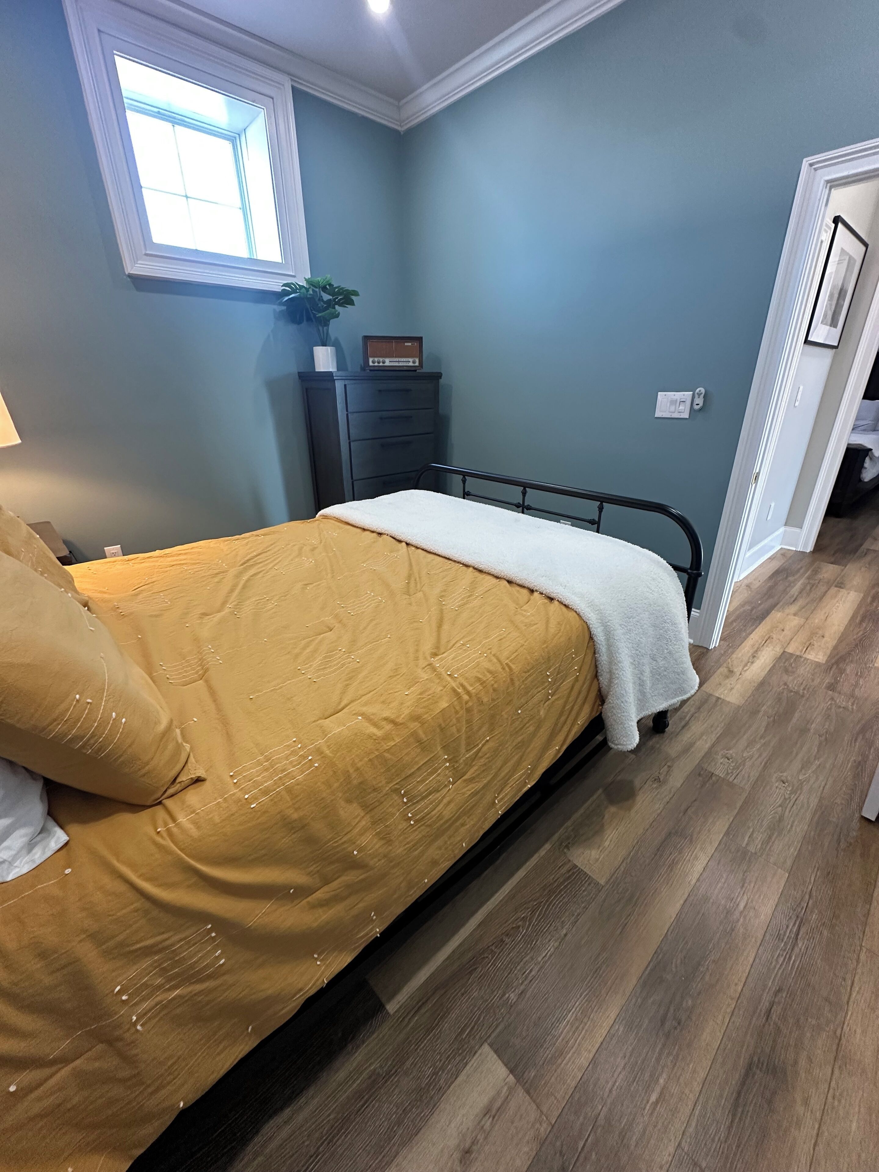 Een slaapkamer met een bed, een dressoir, een raam en een deur.