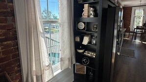 A modern kitchen with a large window, a black bookshelf, and a dining area in the background. - Iuka Downtown Historic King Loft B (Iuka)