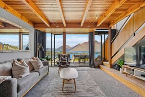 Una sala de estar moderna con un amplio ventanal que ofrece una vista panorámica de montañas y un lago.