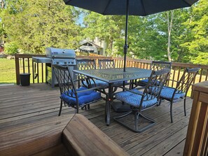 Eine Terrasse im Freien mit Grill, einem runden Tisch mit Stühlen und einer Holzbank.