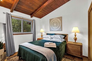 A bedroom with a bed, two bedside tables, a window with curtains, a plant, and a painting on the wall. - 2BR Cozy Cabin Vibes | King Bed + Vaulted Ceilings (Cheyenne)