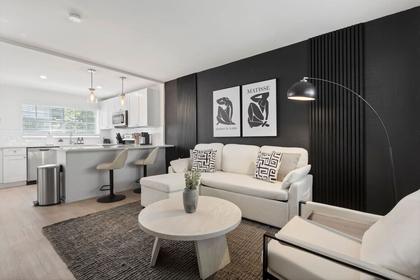 A modern living room with a sofa, armchairs, a coffee table, and a kitchen area in the background.