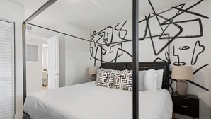 A bedroom with a four-poster bed, a nightstand with a lamp, and abstract wall art. - Luxury apt w/ FREE parking, crib, prime location (Tampa)