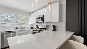 A modern kitchen with white cabinetry, a large island, stainless steel appliances, and pendant lighting. - Luxury apt w/ FREE parking, crib, prime location (Tampa)