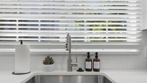 A modern kitchen with a stainless steel sink, white countertops, and a window with horizontal blinds. - Luxury apt w/ FREE parking, crib, prime location (Tampa)
