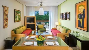 A modern hotel room with a dining area, two sofas, a TV, and artwork on the walls. - New Year's- Dec 27th-Jan 3/2026- Luxury Resort- 2BR Grand Mayan Playa del Carmen (Solidaridad)