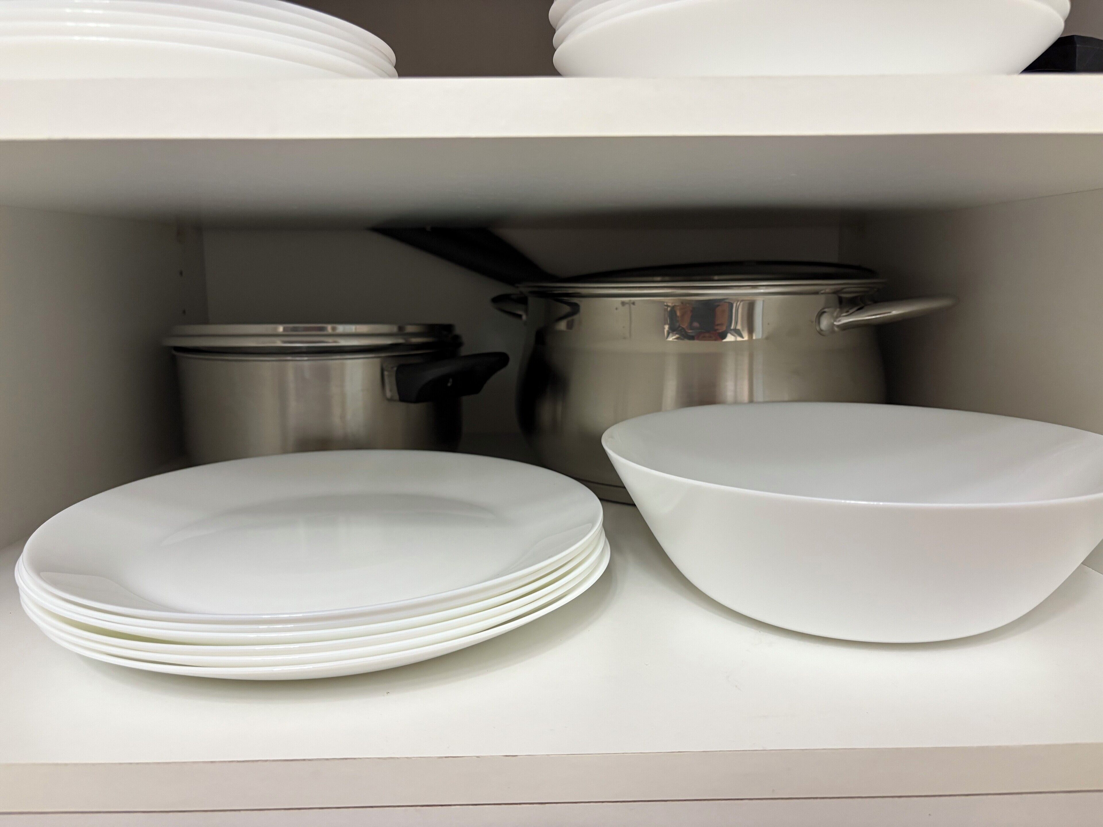 Une étagère de cuisine avec des assiettes blanches, des bols et des casseroles en acier inoxydable.