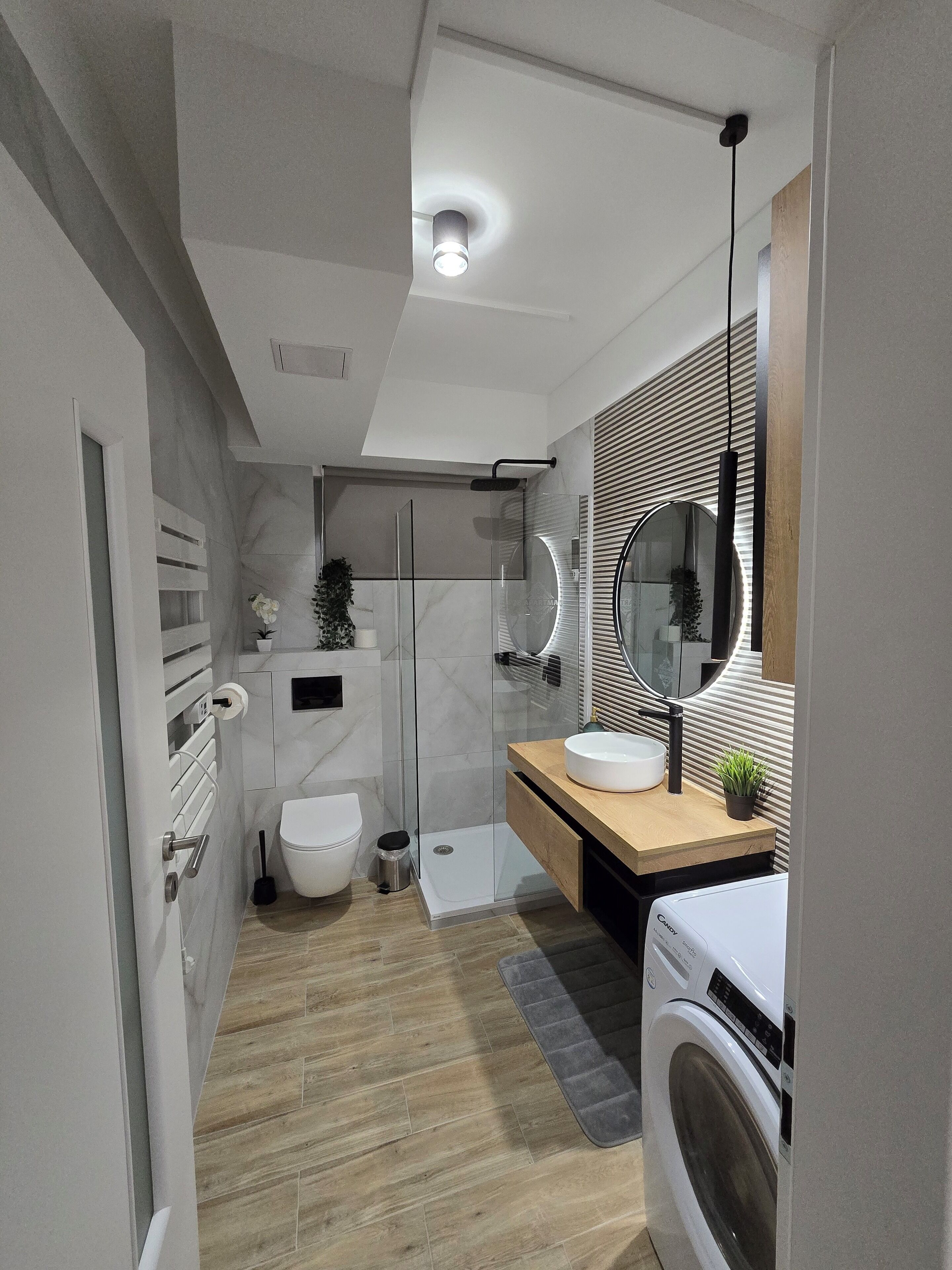 A modern bathroom with a glass shower enclosure, a toilet, a sink with a mirror, and a washing machine.