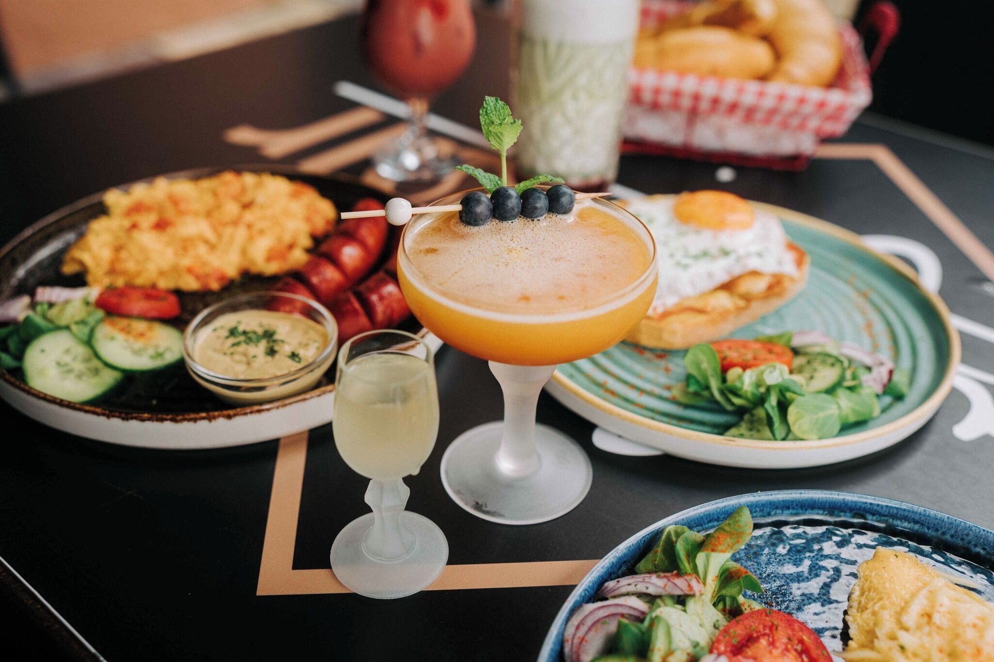 A table with various dishes including a salad, a plate of sausages, a plate of scrambled eggs, and a drink with a garnish.